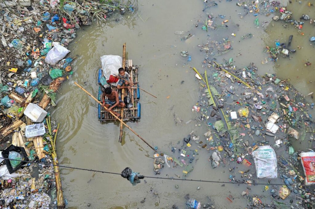 A Father And Son Are Rowing On A Hand Made Raft Searching For Waste Plastic Recycling Products From.jpeg